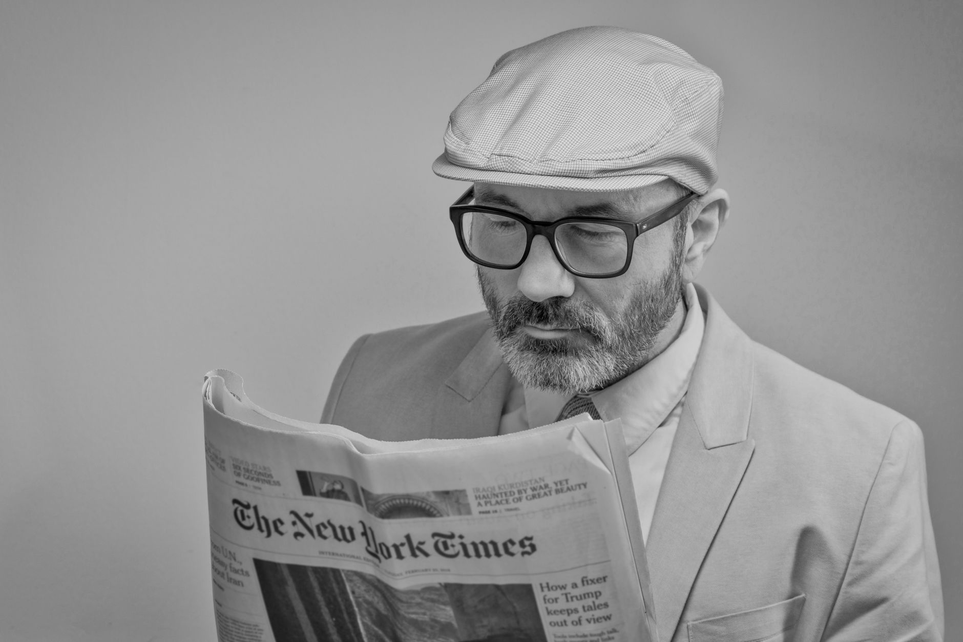 A man in a suit, wearing glasses and a cap, reads The New York Times. — How Aston Martin Shapes Innovation in Formula 1 and A