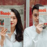 Asian couple playfully posing with Hanoi newspapers indoors, capturing love and connection. — How to Redeem Promo Codes on OK