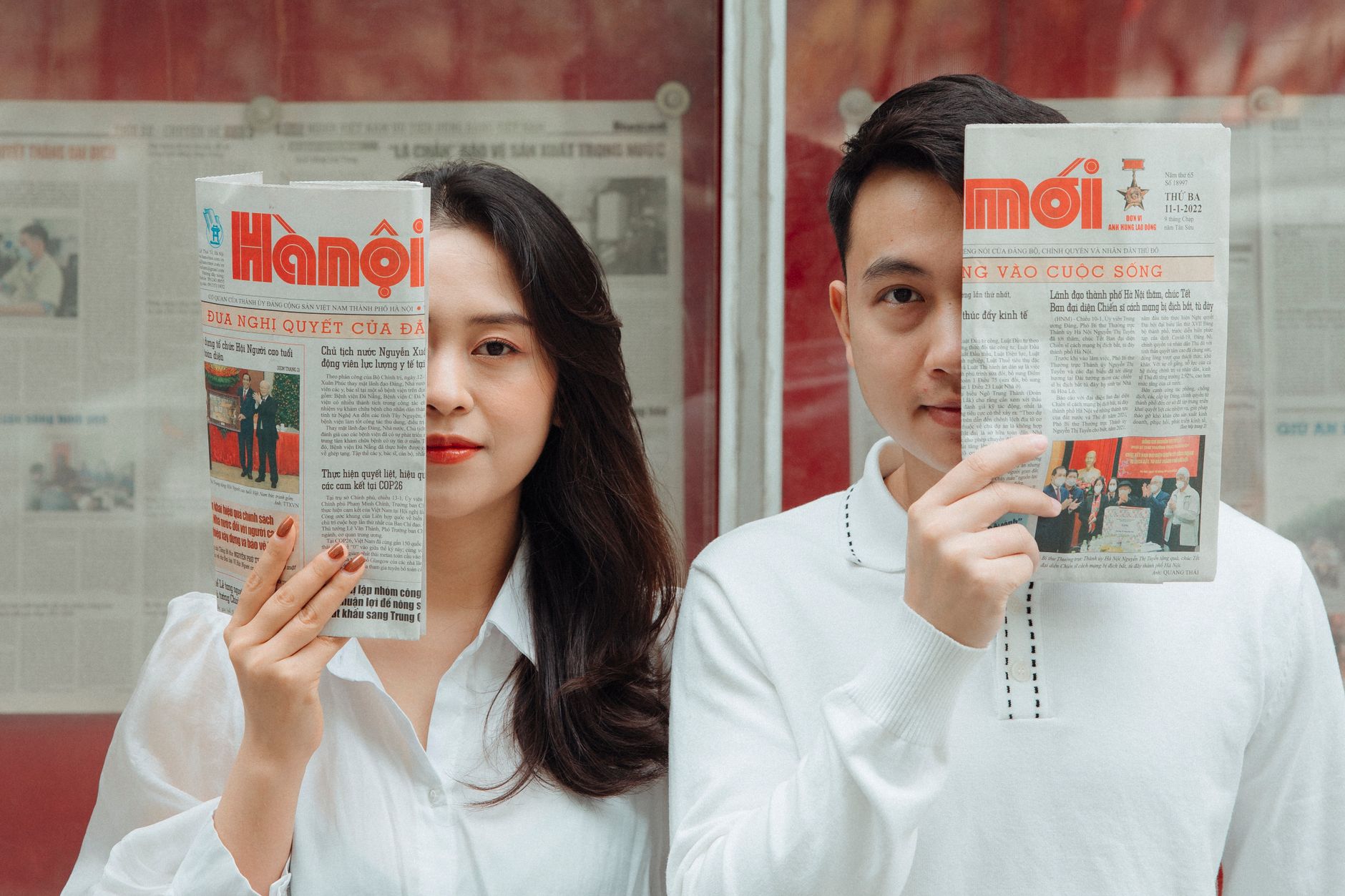 Asian couple playfully posing with Hanoi newspapers indoors, capturing love and connection. — How to Redeem Promo Codes on OK