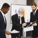 Three businessmen in suits reviewing reports and graphs during an office meeting. — Why Partnering with a Patent Lawyer is Ke