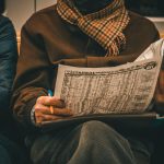 An adult man reads a newspaper showing Istanbul train schedules while sitting indoors. — Why Streameast is Perfect for NFL Fa