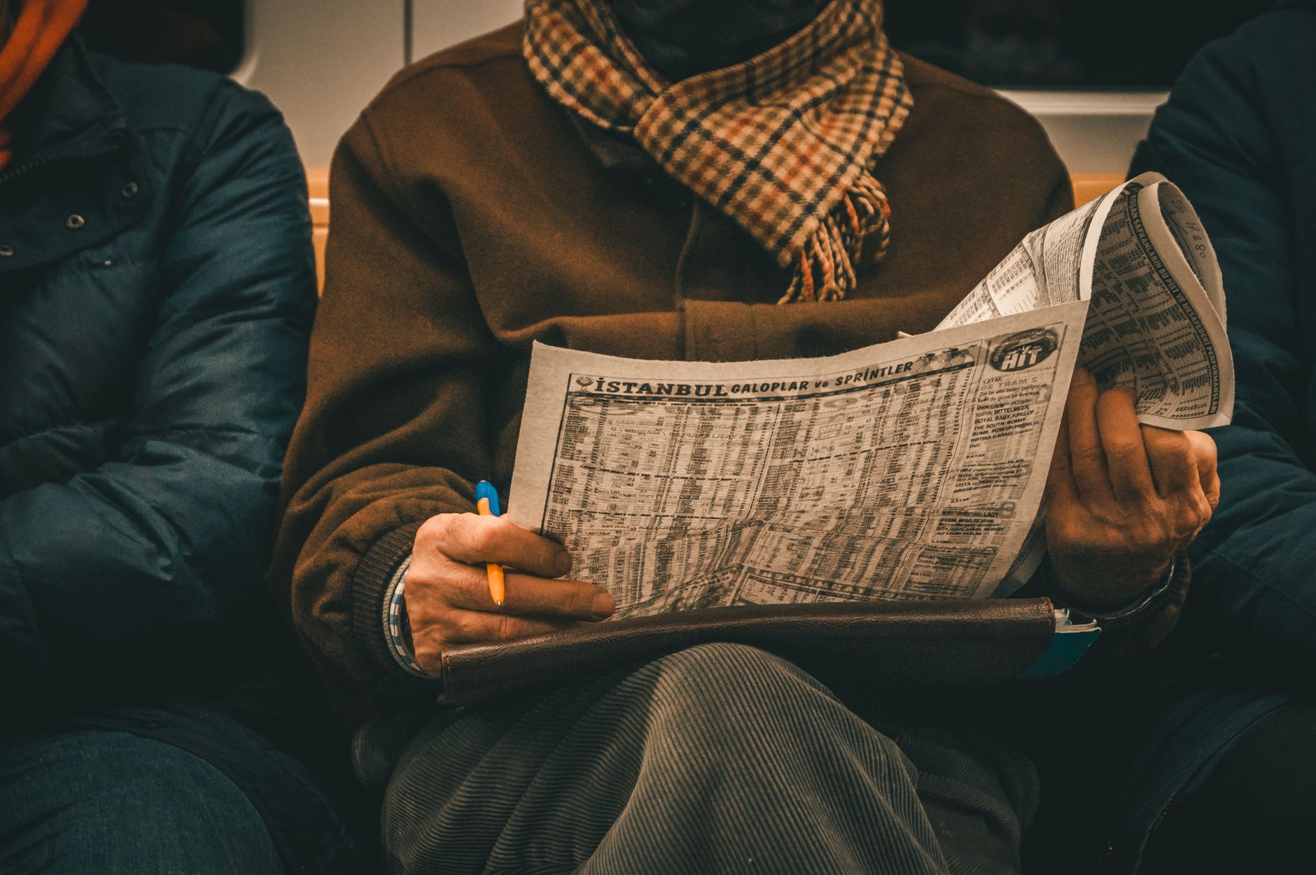 An adult man reads a newspaper showing Istanbul train schedules while sitting indoors. — Why Streameast is Perfect for NFL Fa