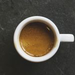 a top-down view of a small cup of espresso on a dark countertop